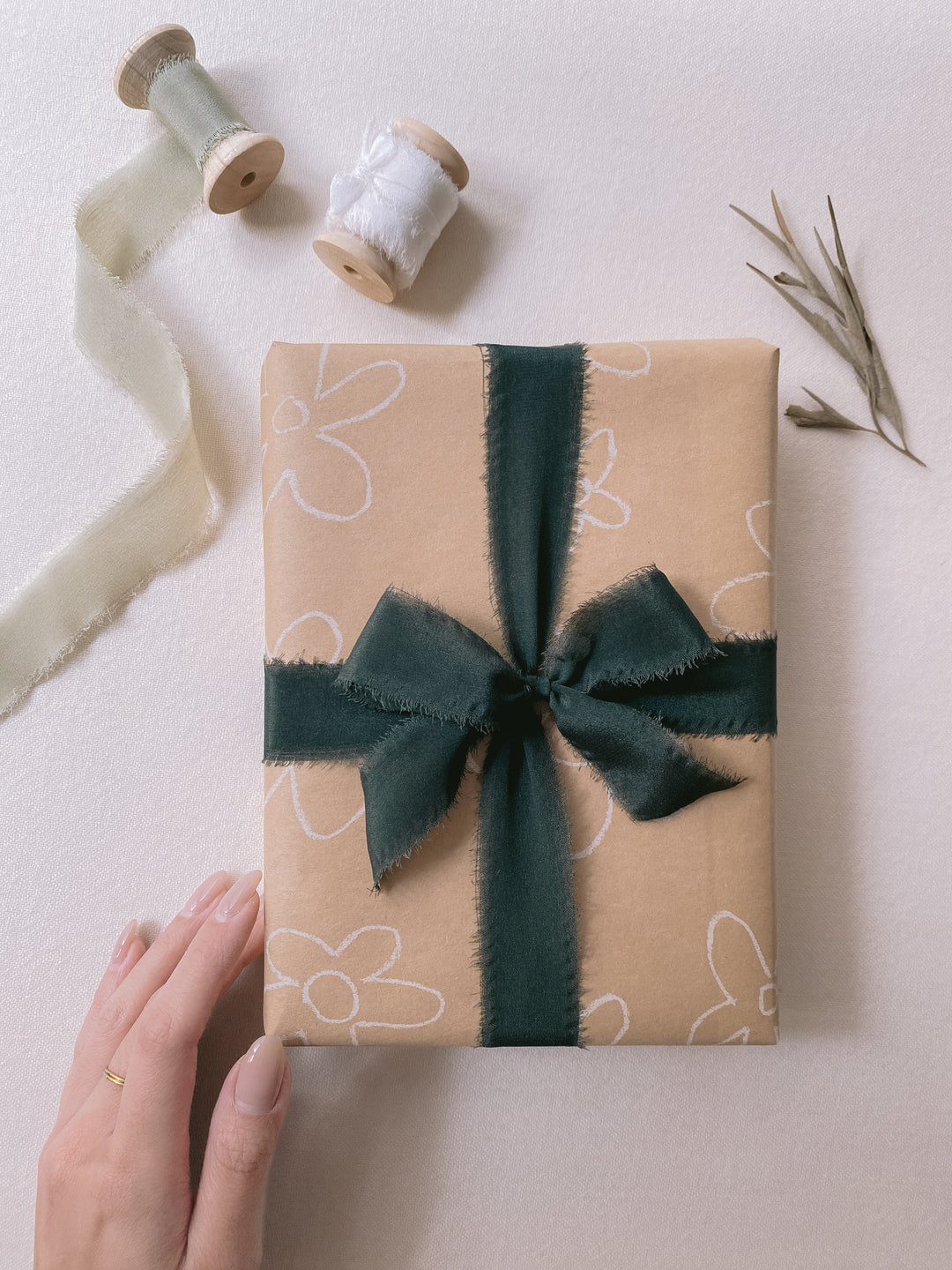 Christmas gift wrapped in dark green silk ribbon and sage green and white silk ribbon with wooden spools