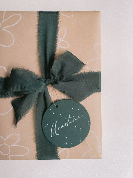 Gift wrapped in Christmas silk ribbon in dark green adorned with round gift tag in deep green 