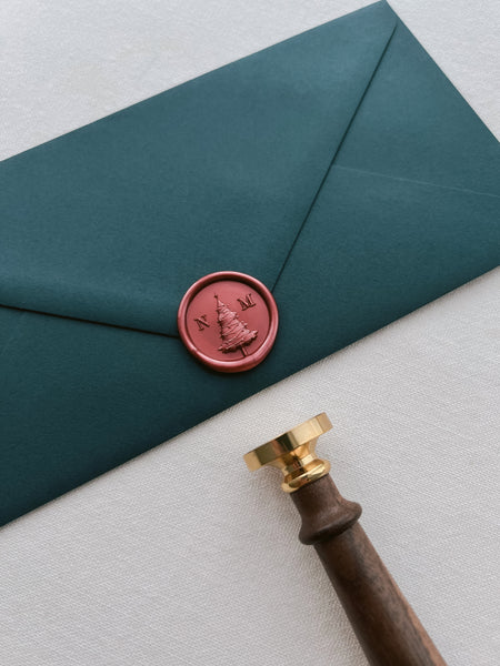 Red Christmas tree monogram wax seal with personalised initials on a dark green envelope
