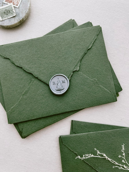 Custom monogram Christmas tree design silver wax seal on a stack of green handmade paper envelopes 