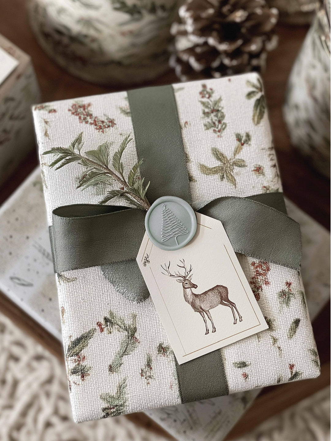 Light sage green Christmas tree wax seal on a wrapped Christmas gift decorated with silk ribbon