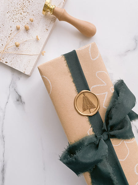 Christmas tree wax seal in gold on gift wrapped with beige flower gift wrapping paper