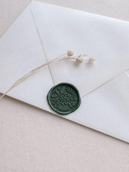 dark green Christmas wax seal featuring design of winter botanicals and snowflakes