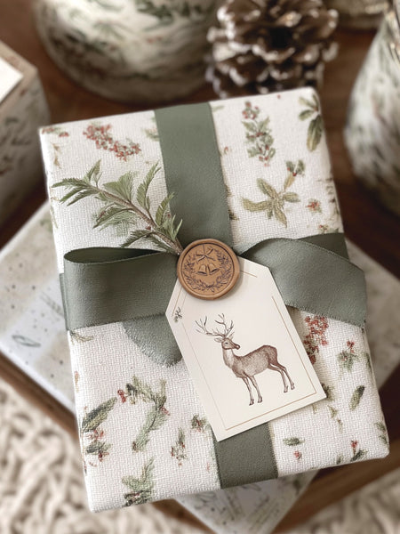 Gold Christmas wreath wax seal on a wrapped holiday gift decorated with green silk ribbon and reindeer gift tag