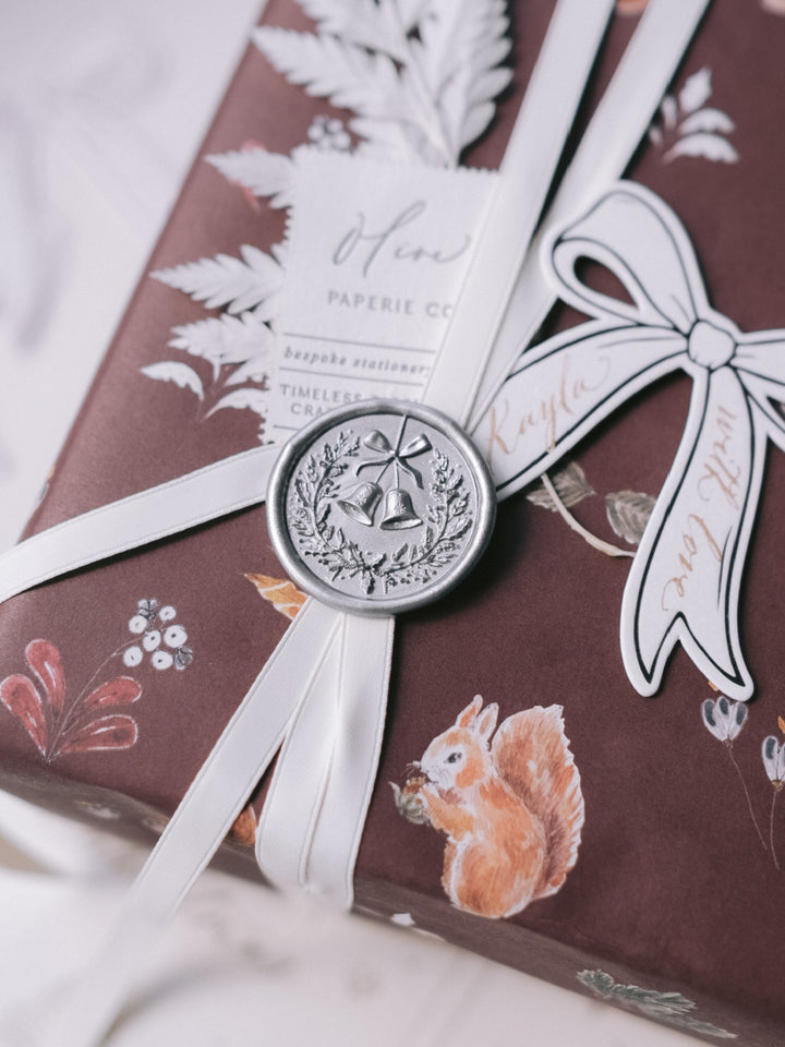 Silver 3D Christmas wreath wax seal on a present wrapped in brown festive wrapping paper with a personalized bow shaped gift tag