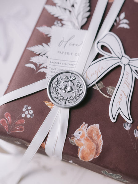 Silver Christmas wreath and jingle bells wax seal on a wrapped holiday gift box