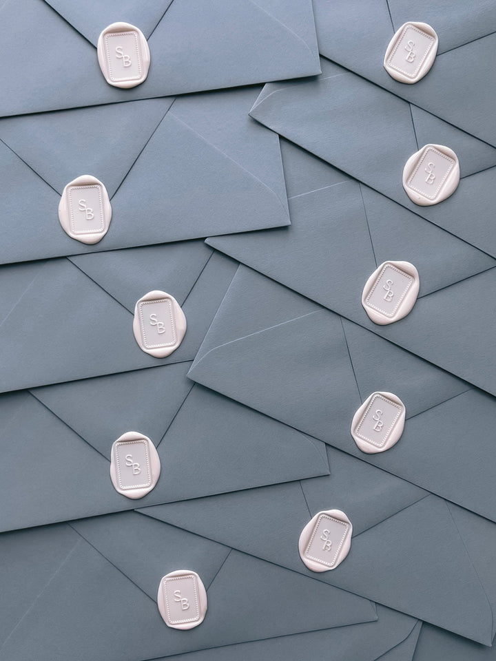 Rectangular dotted border monogram wax seals in ivory nude on dusty blue envelopes