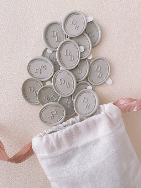 Light gray oval monogram wax seal stickers with a white linen pouch with pink drawstrings