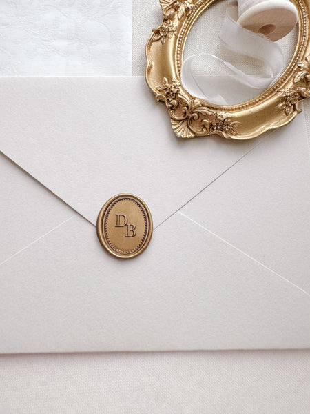 Custom monogram oval gold wax seal with a dotted border design on a light beige envelope