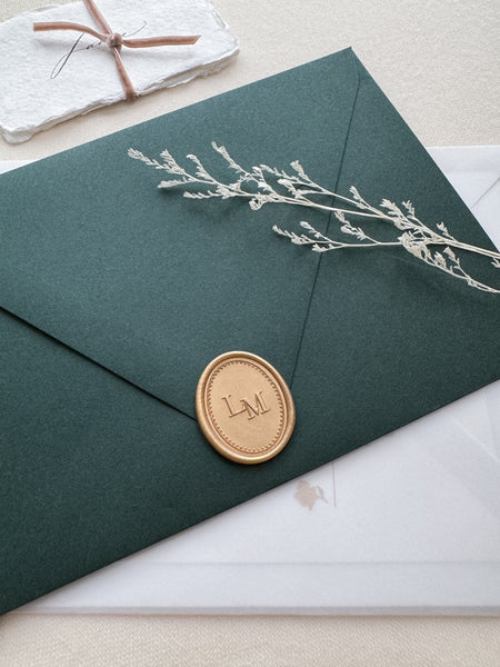 Custom monogram oval light gold wax seal with a dotted border design on a dark green envelope