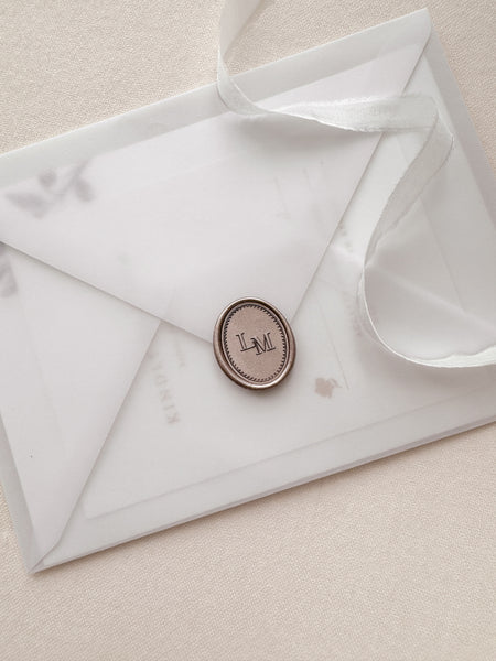 Custom monogram oval wax seal in color mocha with a dotted border design on a vellum envelope
