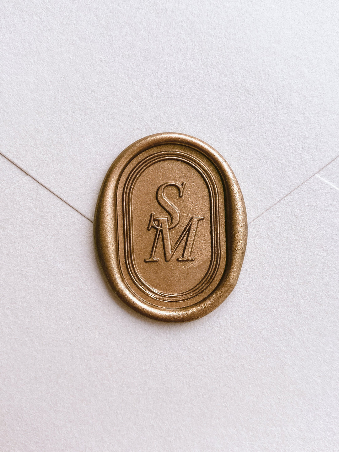 Oval gold custom wax seal with personalized monogram letter and double line border design on white card stock envelope