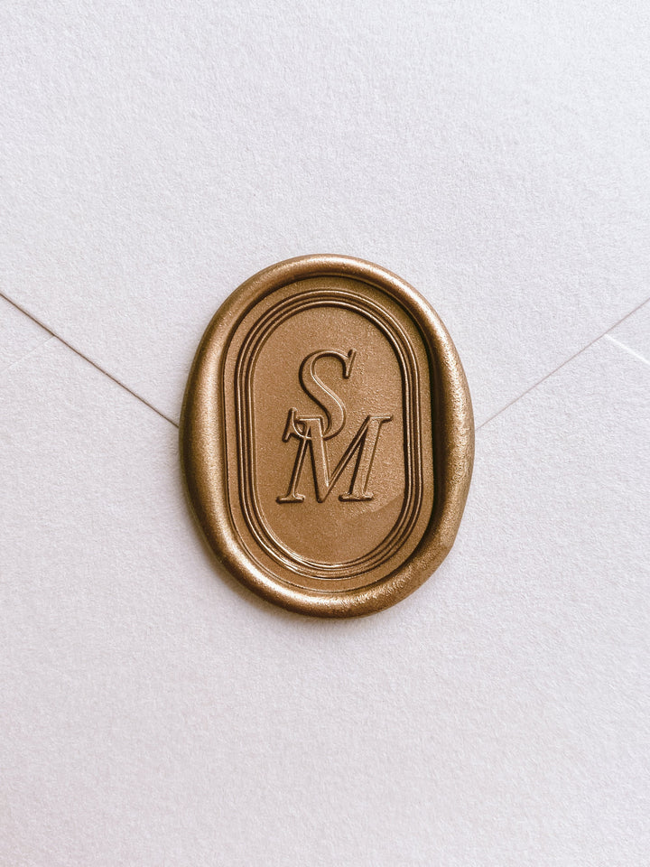 Oval gold custom wax seal with personalized monogram letter and double line border design on white card stock envelope