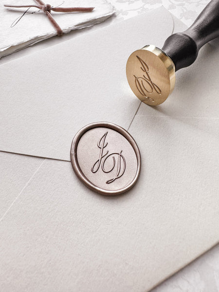 Custom calligraphy script monogram wax seal in a light bronze color on a beige envelope