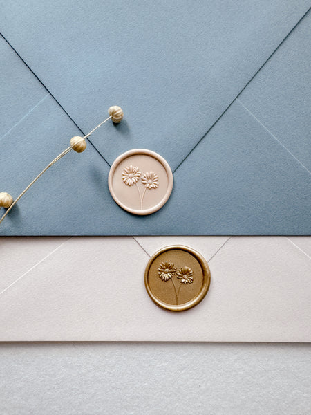 Gold and nude daisies wax seals on dusty blue and beige envelopes
