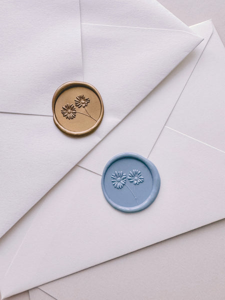 Gold and dusty blue wax seals featuring a design of daisies with 3D engravings on white envelopes