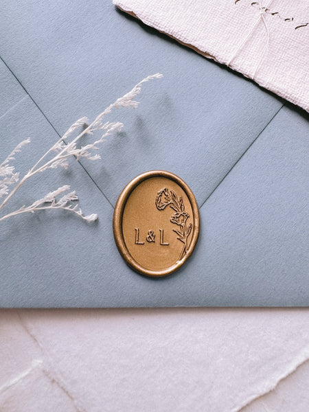 Oval floral custom monogram gold wax seal on a dusty blue envelope