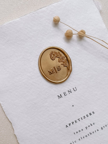 Oval floral monogram gold custom wax seal on white handmade paper menu styled with dried flowers