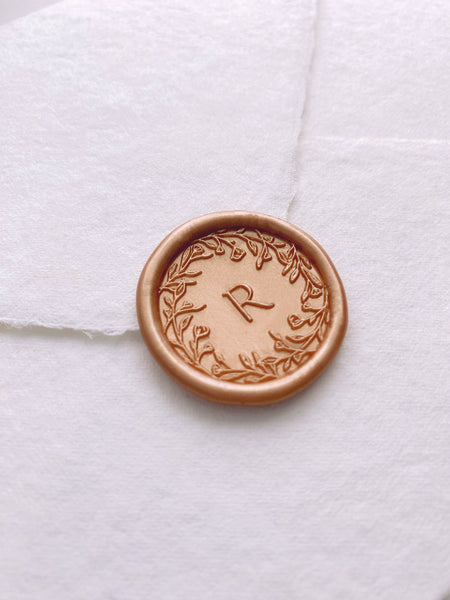floral crown single initial wax seal in peachy gold color on white handmade paper envelope side angle