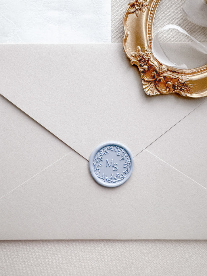 Floral wreath design monogram wax seal in color pale blue on a light beige envelope