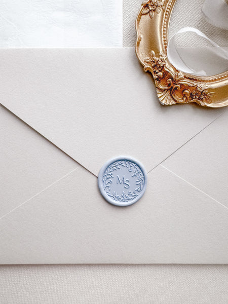 Floral wreath design monogram wax seal in color pale blue on a light beige envelope