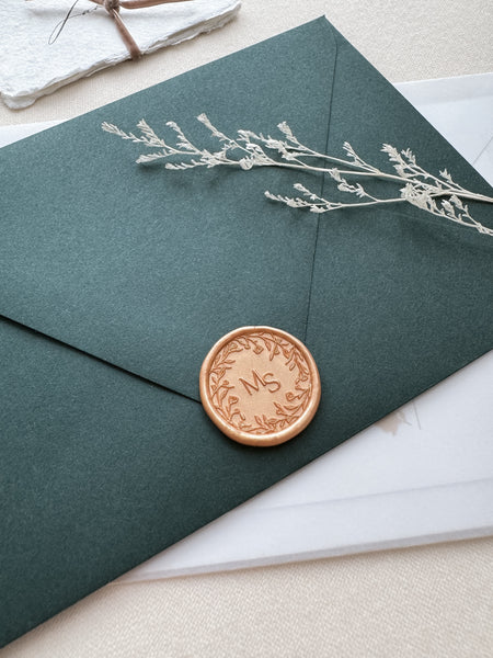 Floral wreath design monogram wax seal in color peachy gold on a dark green envelope