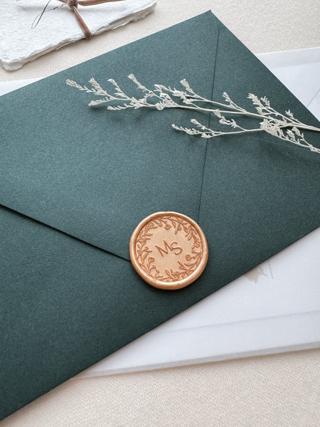 Floral wreath design monogram wax seal in color peachy gold on a dark green envelope