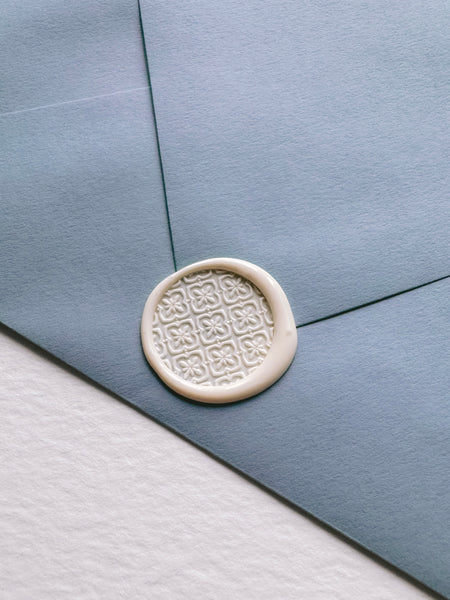 Moroccan tile pattern round wax seal in off-white color on a dusty blue envelope