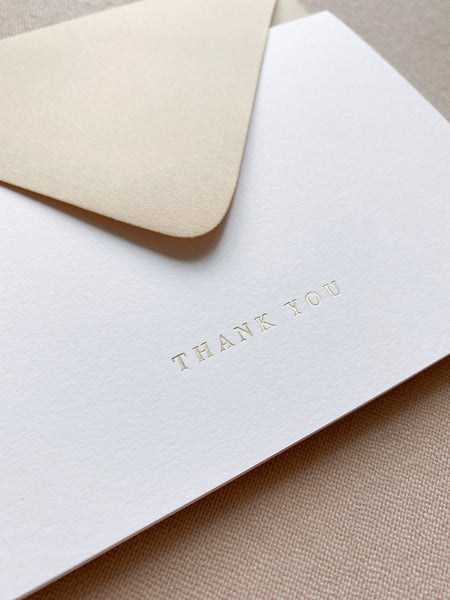 gold foil pressed white thank you card with a beige envelope 