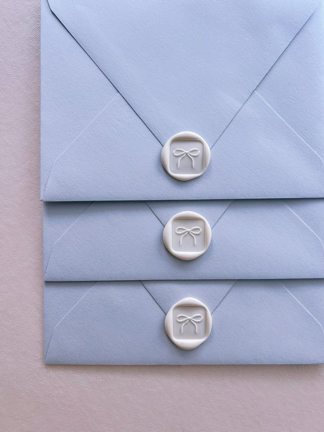 white 3D ribbon bow mini square wax seal on a light blue envelopes
