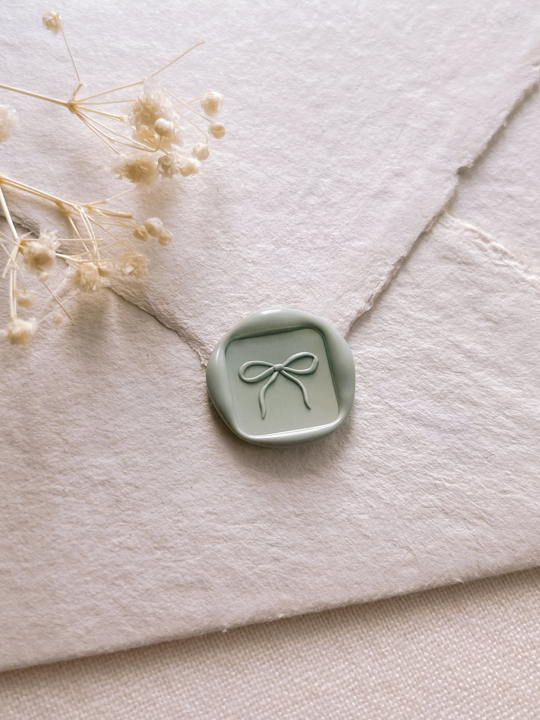 light sage green 3D hand-drawn ribbon bow mini square wax seal on an off-white textured envelope