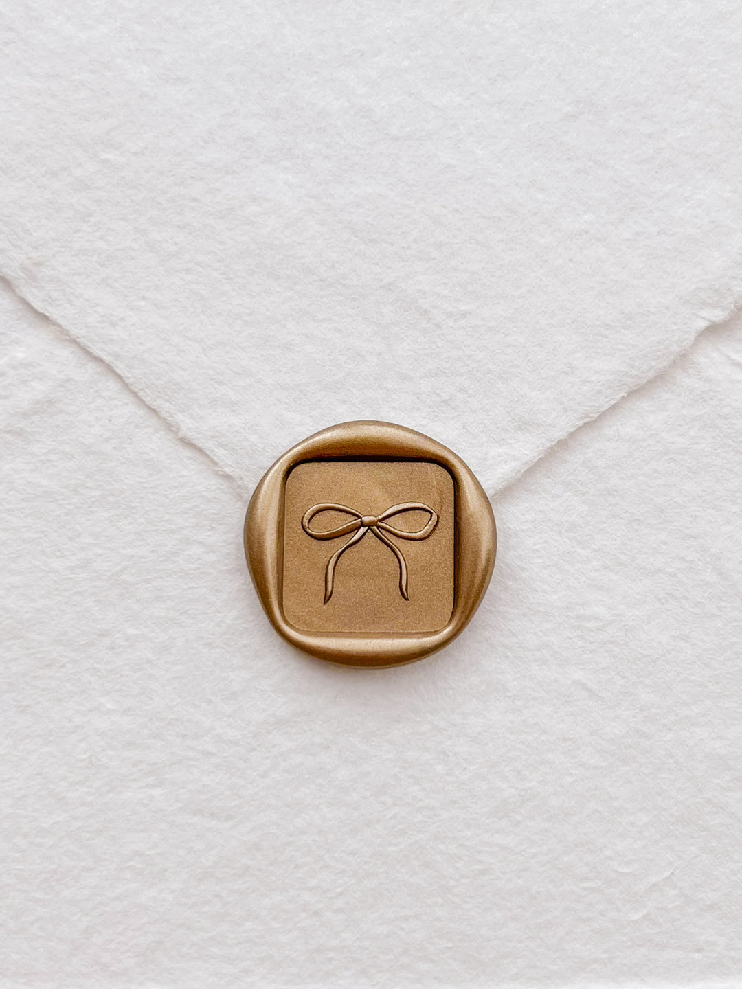 gold ribbon  bow square wax seal on a white handmade paper envelope