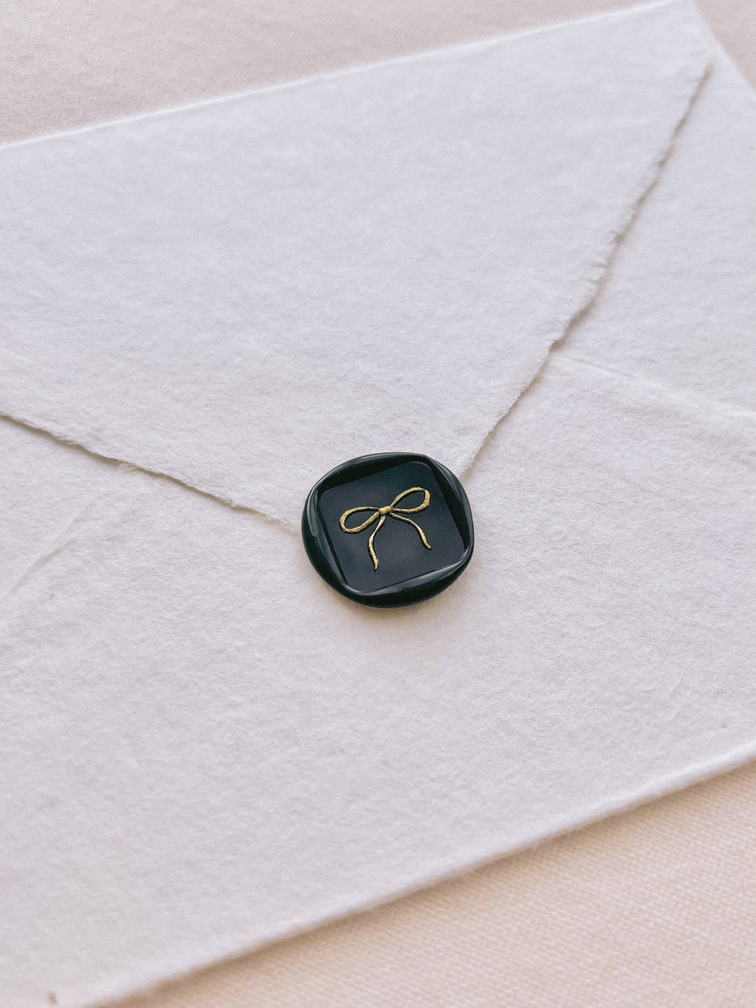 square shaped hand-drawn bow design wax seal in black with the design painted in gold 