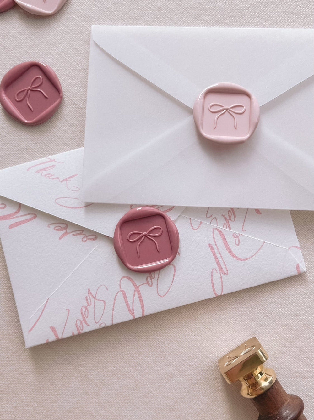 Dusty rose and pink ribbon bow design wax seals on white and clear envelopes 