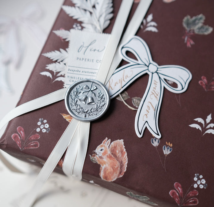 Silver festive wax seal featuring a Christmas wreath and jingle bells design on a wrapped gift and personalized gift tag
