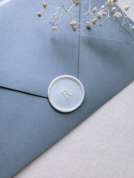 pearl colored custom initial wax seal on a dusty blue envelope