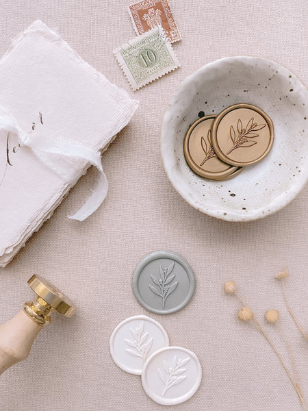 Leaf branch wax seals in light gold, sage green and off white styled with wax seal stamp, wax seals and place cards tied with white silk ribbon
