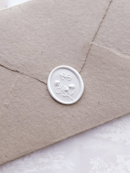 White 3D floral monogram custom wax seal on a light brown handmade paper envelope 