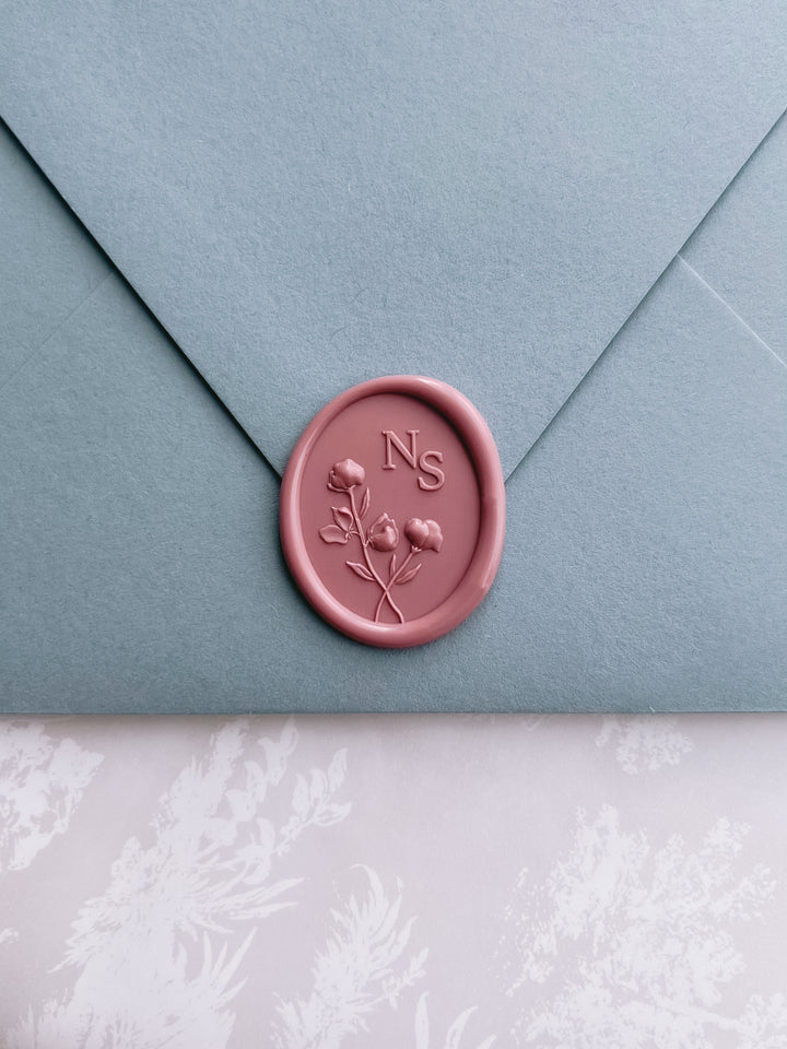 rose colored personalized initials wax seal with 3D floral design on a dusty blue envelope 