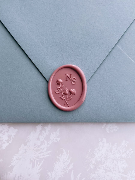 Dusty rose colored custom floral monogram oval wax seal on a dusty blue wedding invitation envelope