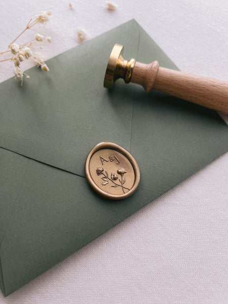Custom flower design monogram oval gold wax seal with personalized initials on an olive green envelope