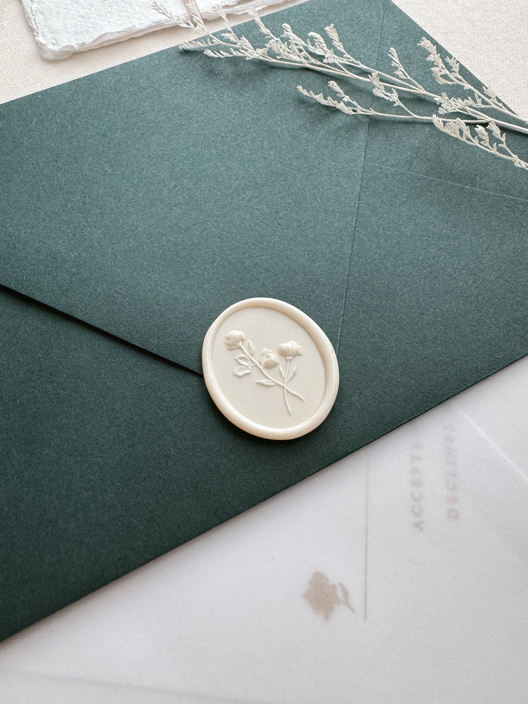 off-white oval flower wax seal on a dark green envelope