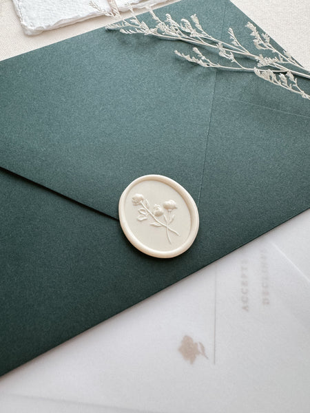 Off-white floral oval wax seal on a dark green wedding invitation envelope