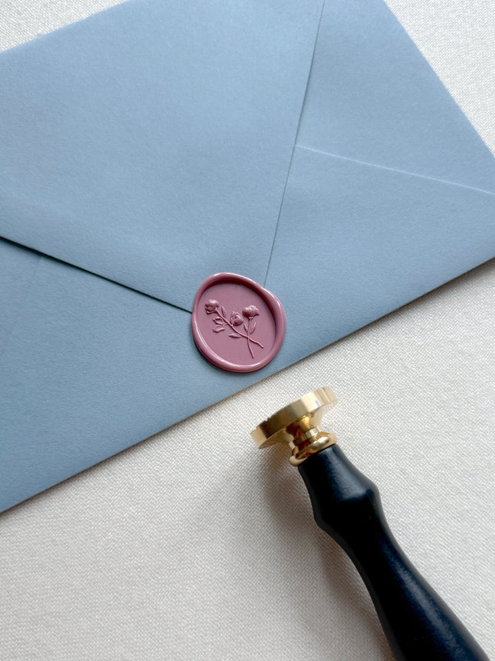 rose colored oval floral wax seal on a dusty blue envelope
