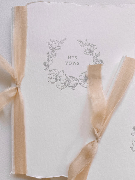 A set of two His and Her letterpress floral wreath vow books with peachy blush colored silk ribbon