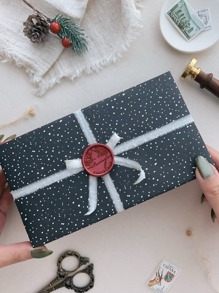 Dark metallic red Merry Christmas wreath design wax seal on a wrapped holiday gift