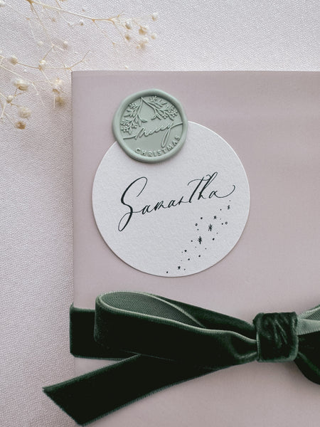 Light pastel green Merry Christmas wreath design wax seal on a wrapped gift box with dark green velvet ribbon