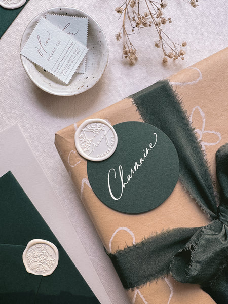 Off-white Merry Christmas wax seal and dark green gift tag with personalized name attached on a gift