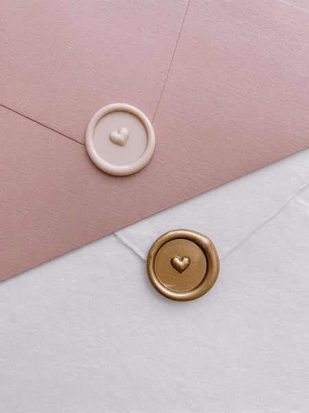 Nude colored mini heart wax seal on a dusty pink envelope and a gold mini heart wax seal on a white handmade paper envelope