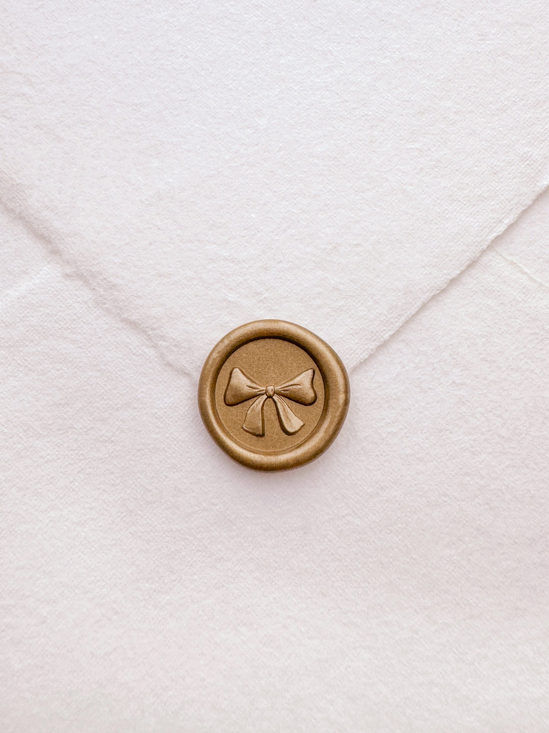 gold 3D ribbon bow mini wax seal on a white textured handmade paper envelope